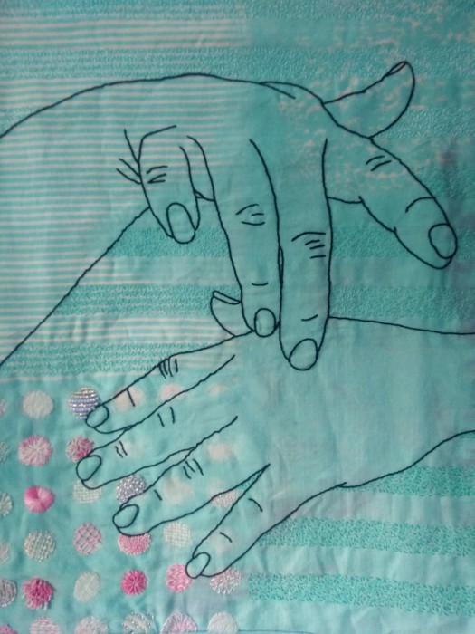 the sign language symbol for touch is stitched in a black outline on a sea green cloth with circles of pink and white textures stitched underneath