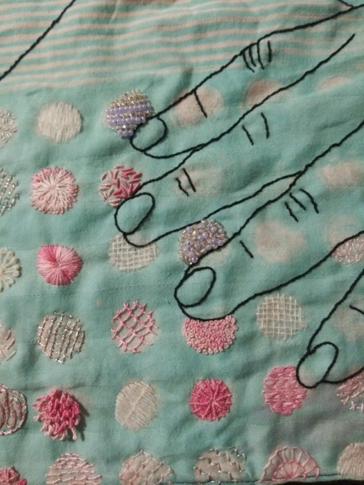 a detail view of pink and white texture stitches and beading inside circles on a sea-green cloth